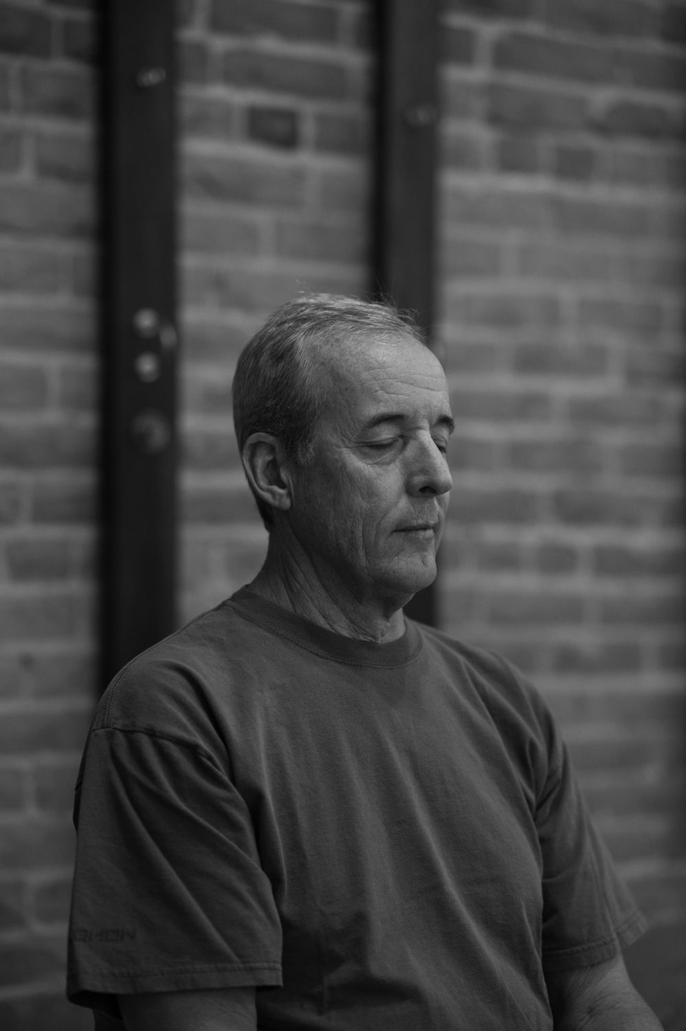 A man is sitting in front of a brick wall with his eyes closed.