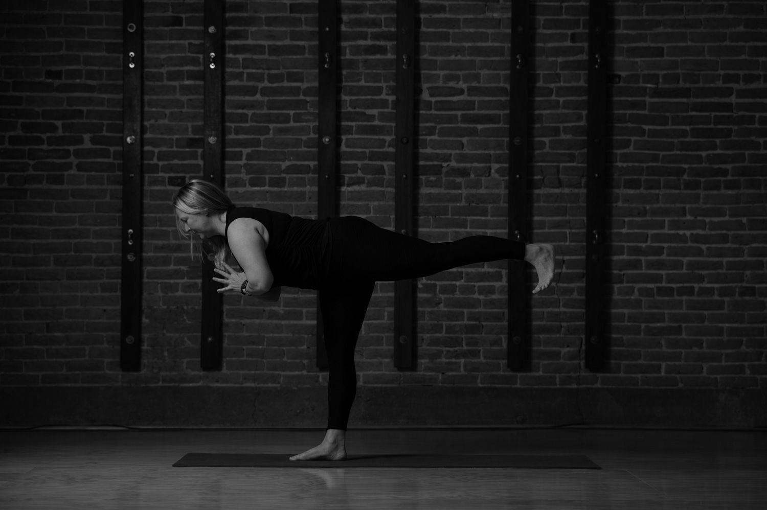 A woman is sitting on a yoga mat in front of a brick wall.