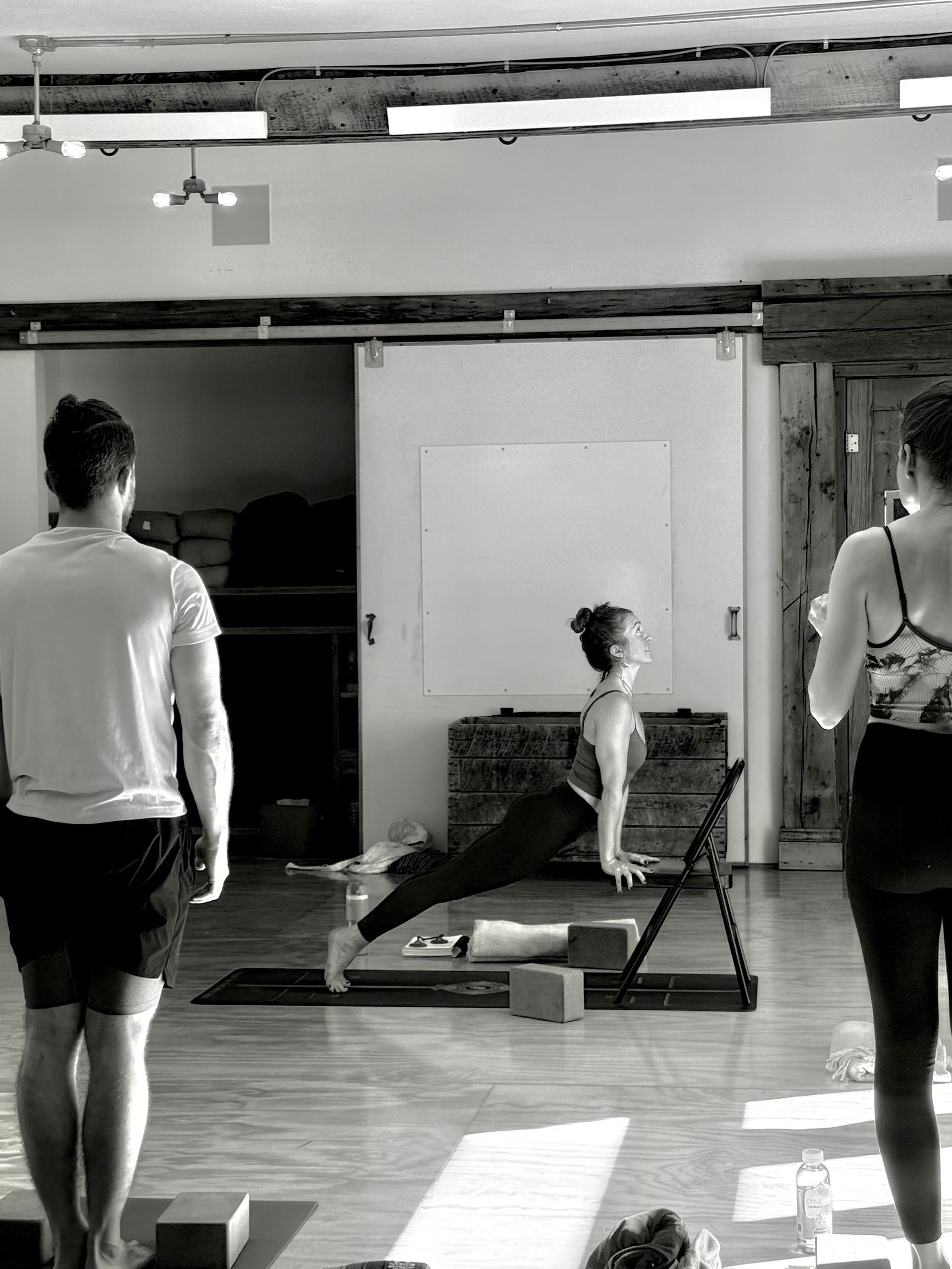 Woman in black athletic wear doing yoga pose with one foot on a chair, reaching arm overhead.