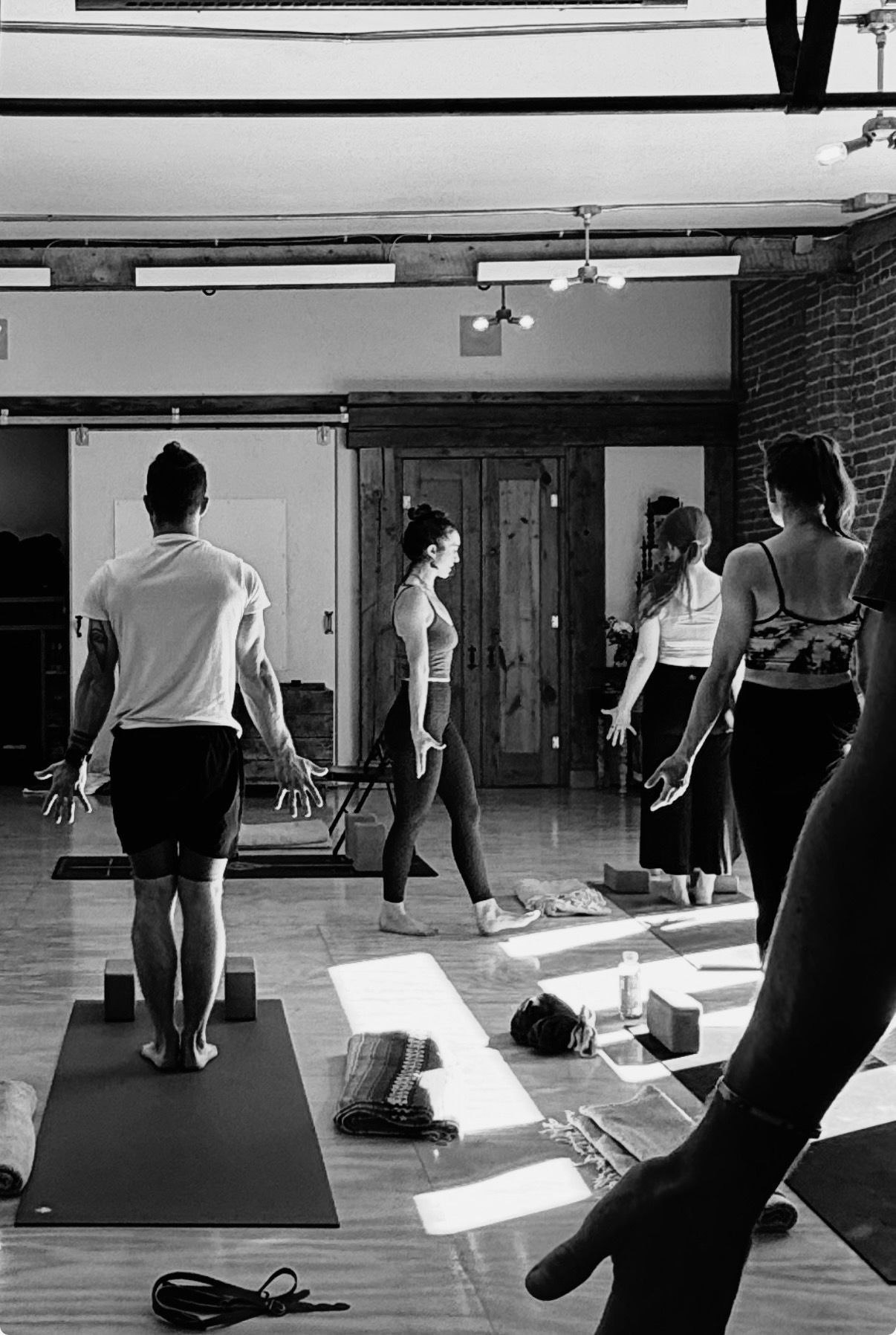 Person balances in a yoga pose, holding ball, one leg extended, on a mat in front of brick wall.