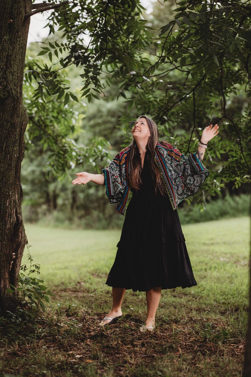 A woman is sitting on a rock with her arms outstretched