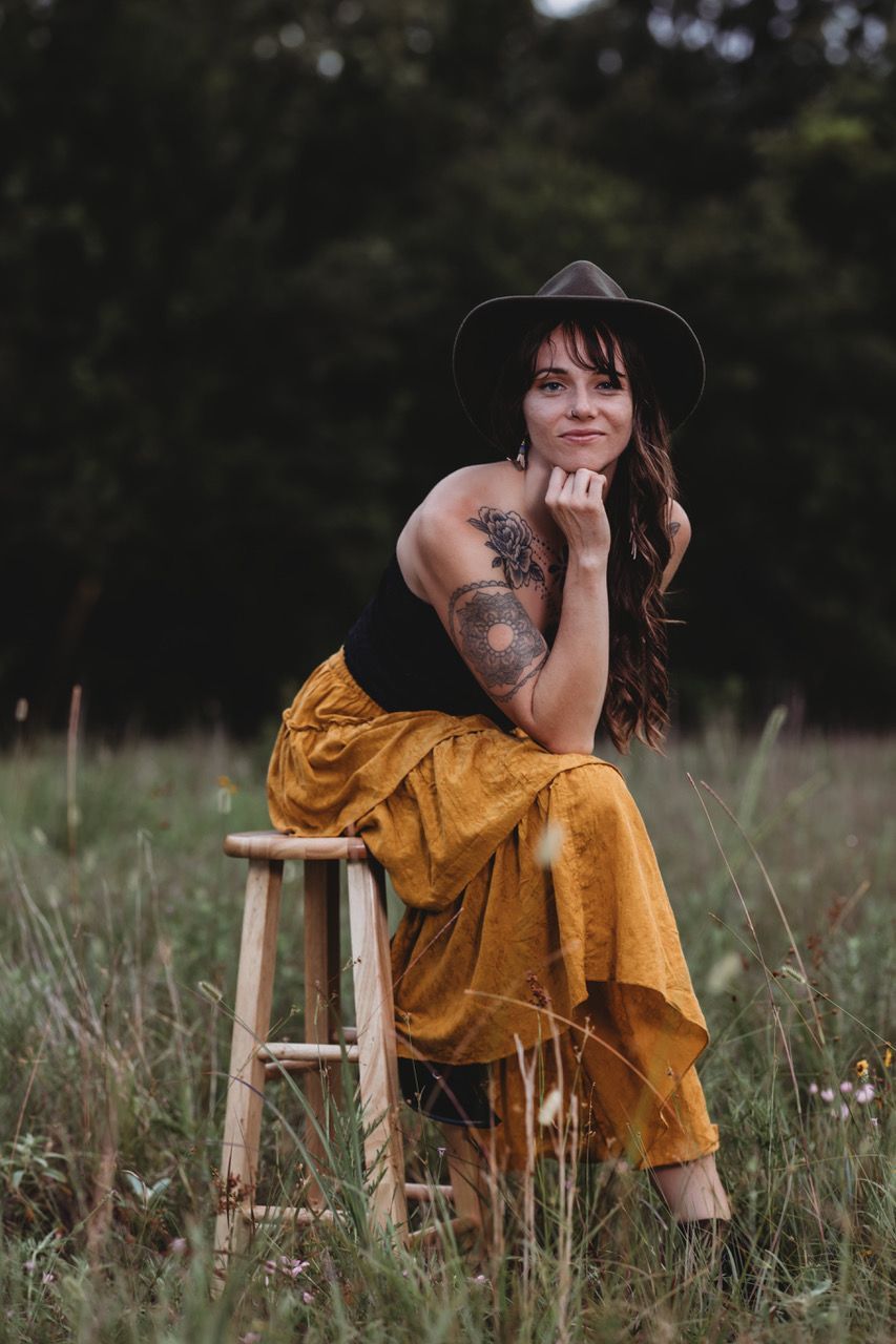 A woman wearing glasses and a scarf is standing in front of a wooden fence.