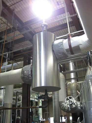 A large metal pipe is hanging from the ceiling of a factory.