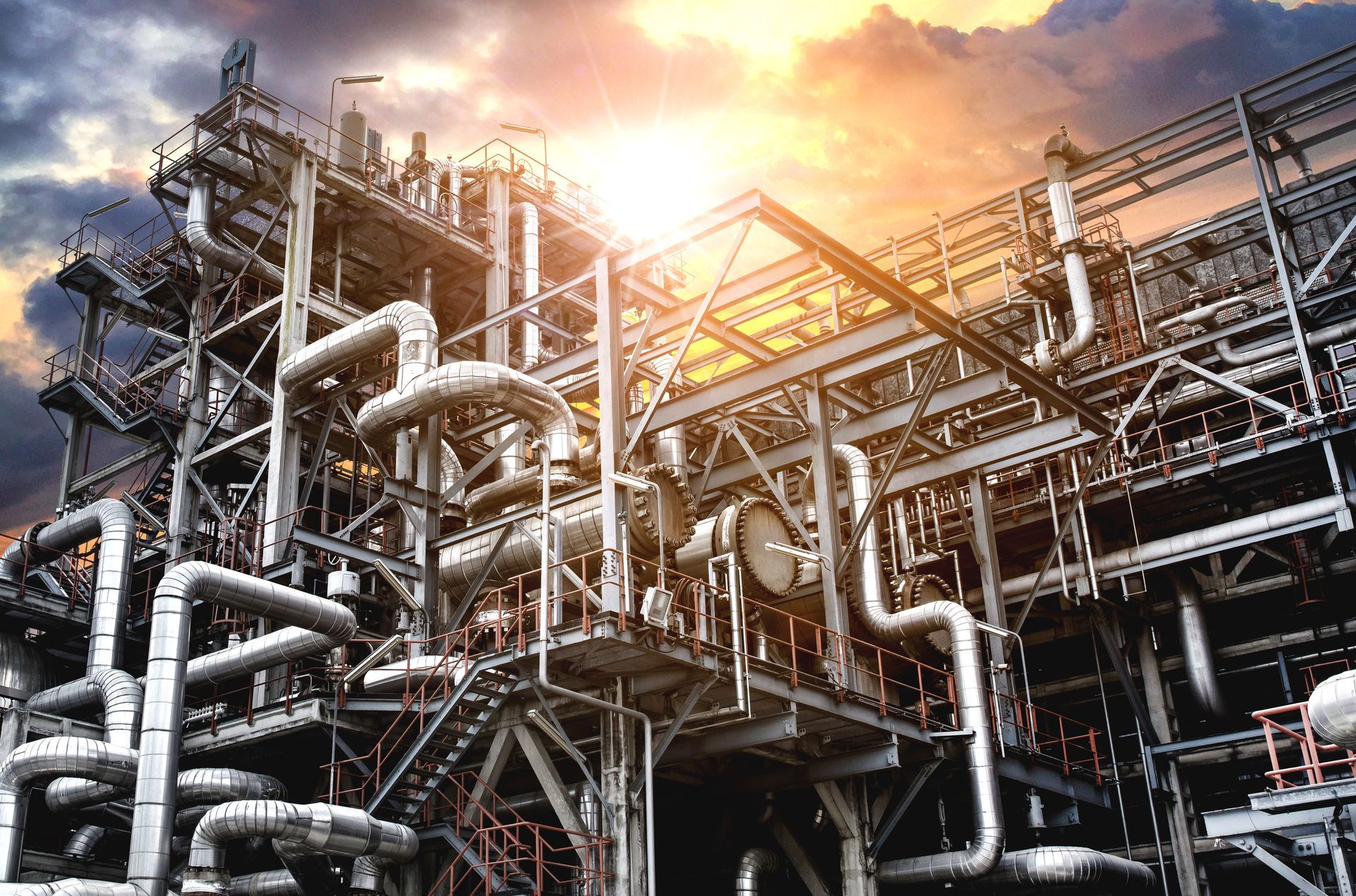 A large industrial plant with pipes and stairs at sunset.