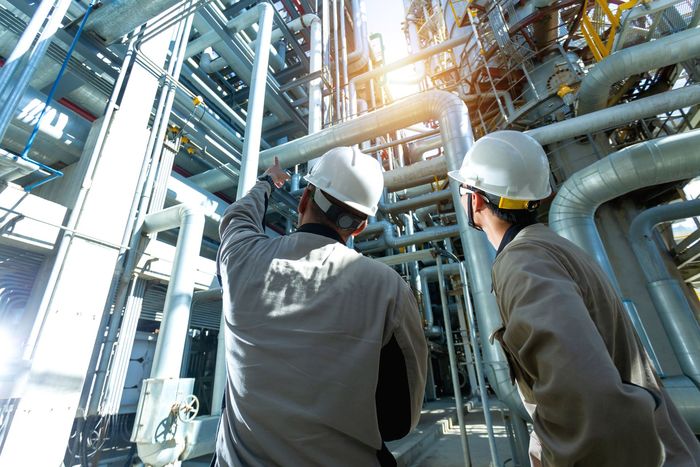 Two men in hard hats are looking at pipes in a factory.