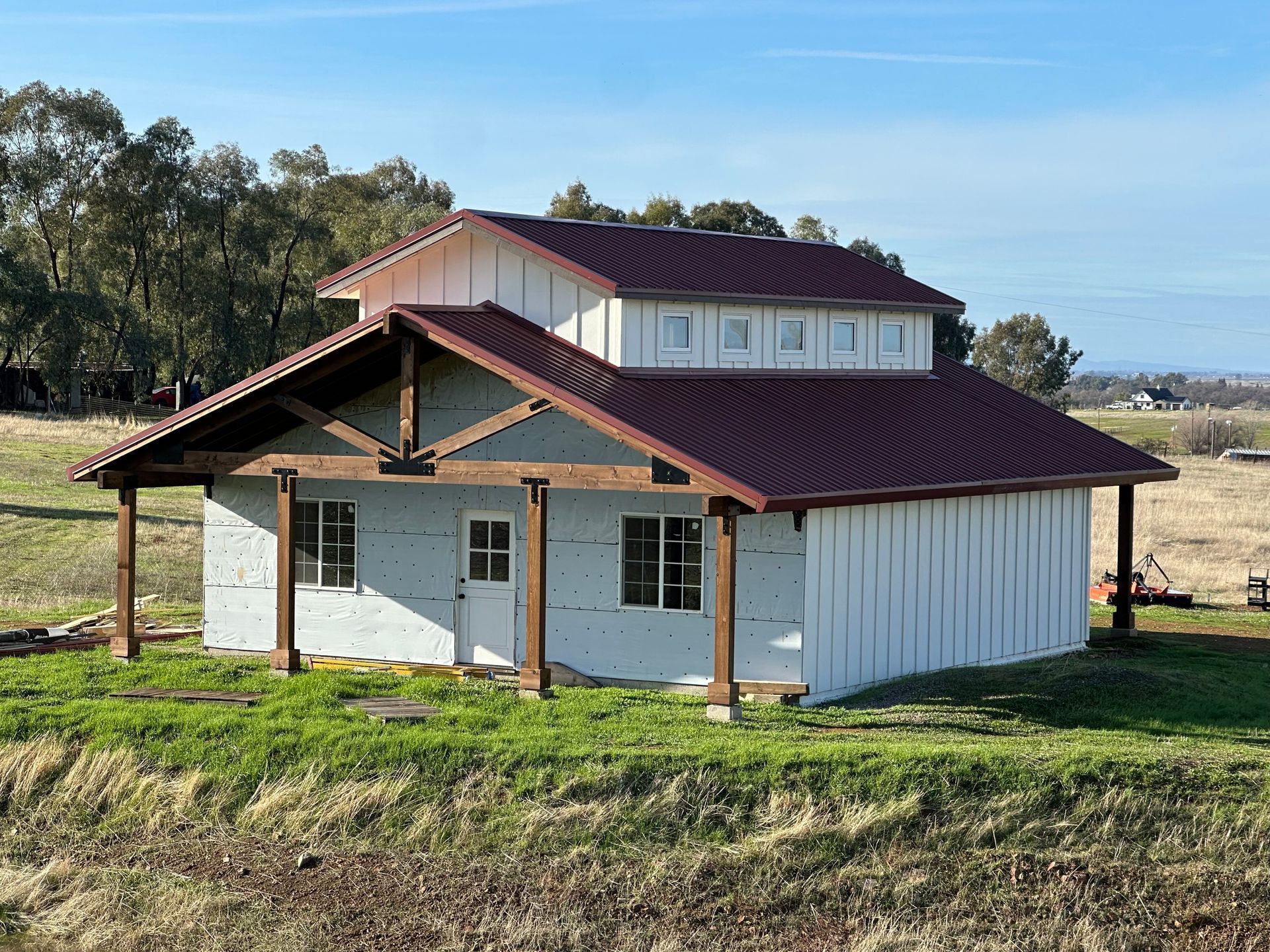 A small white house with a red roof is sitting in the middle of a grassy field.