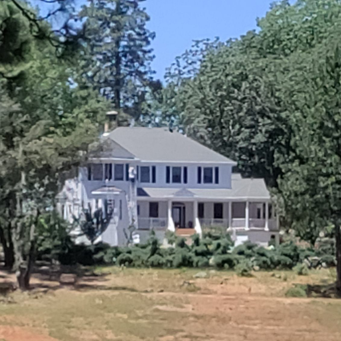 A large white house with a porch is surrounded by trees.