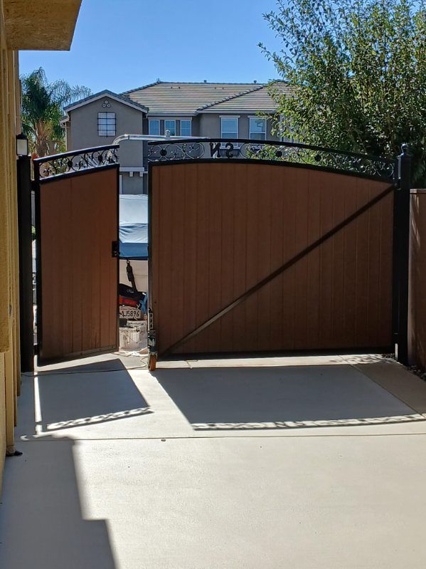 A wooden gate is open to a driveway with a house in the background.