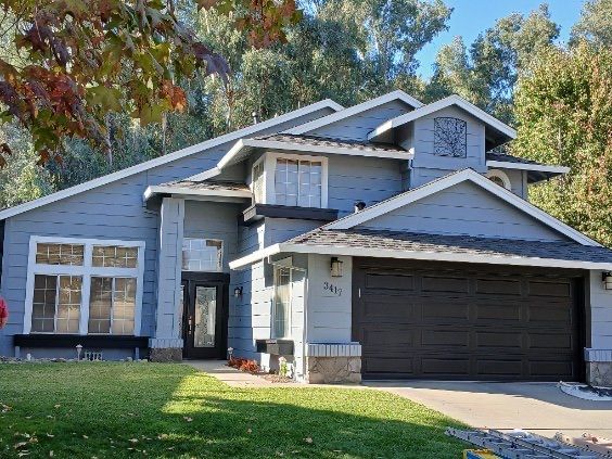 A large blue house with a black garage door is surrounded by trees.