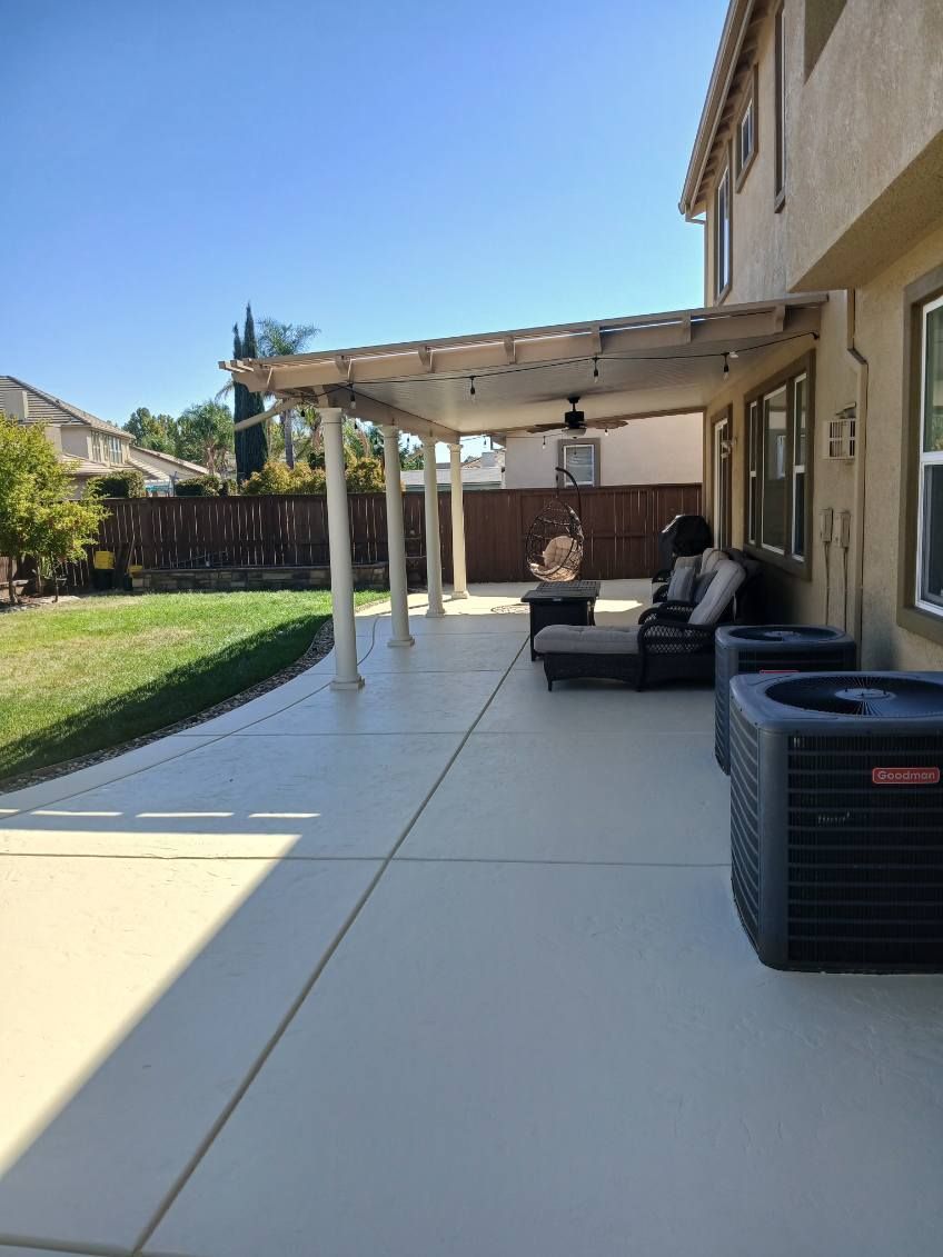 A patio with a couch and chairs under a pergola in the backyard of a house.
