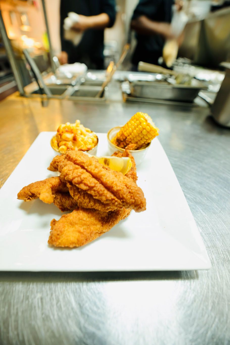 A white plate topped with fried fish , corn on the cob and french fries.