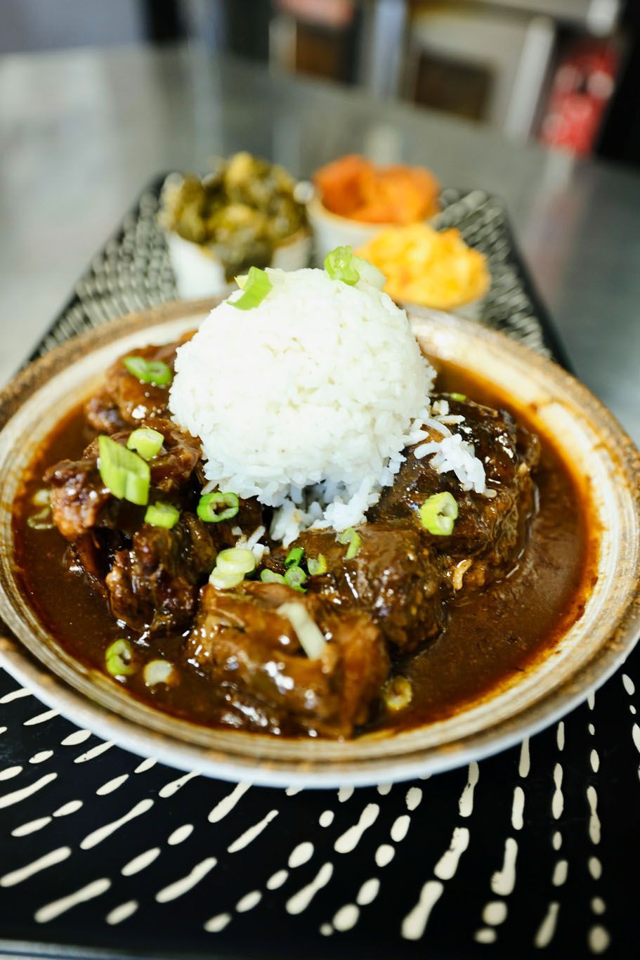 A bowl of stew with rice and green onions on a table.