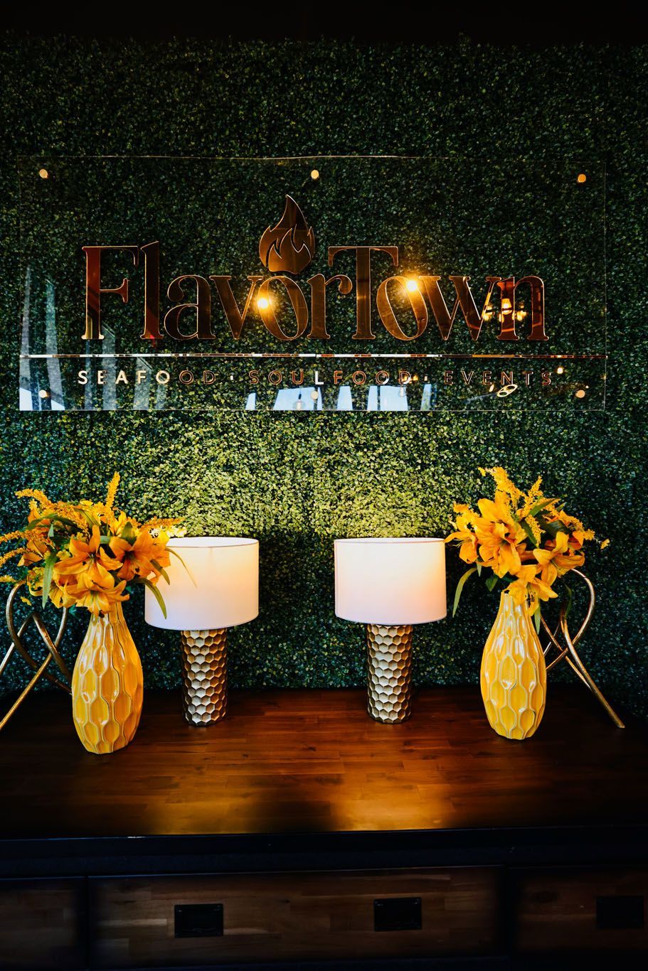 A table with two lamps and vases of yellow flowers in front of a green wall.