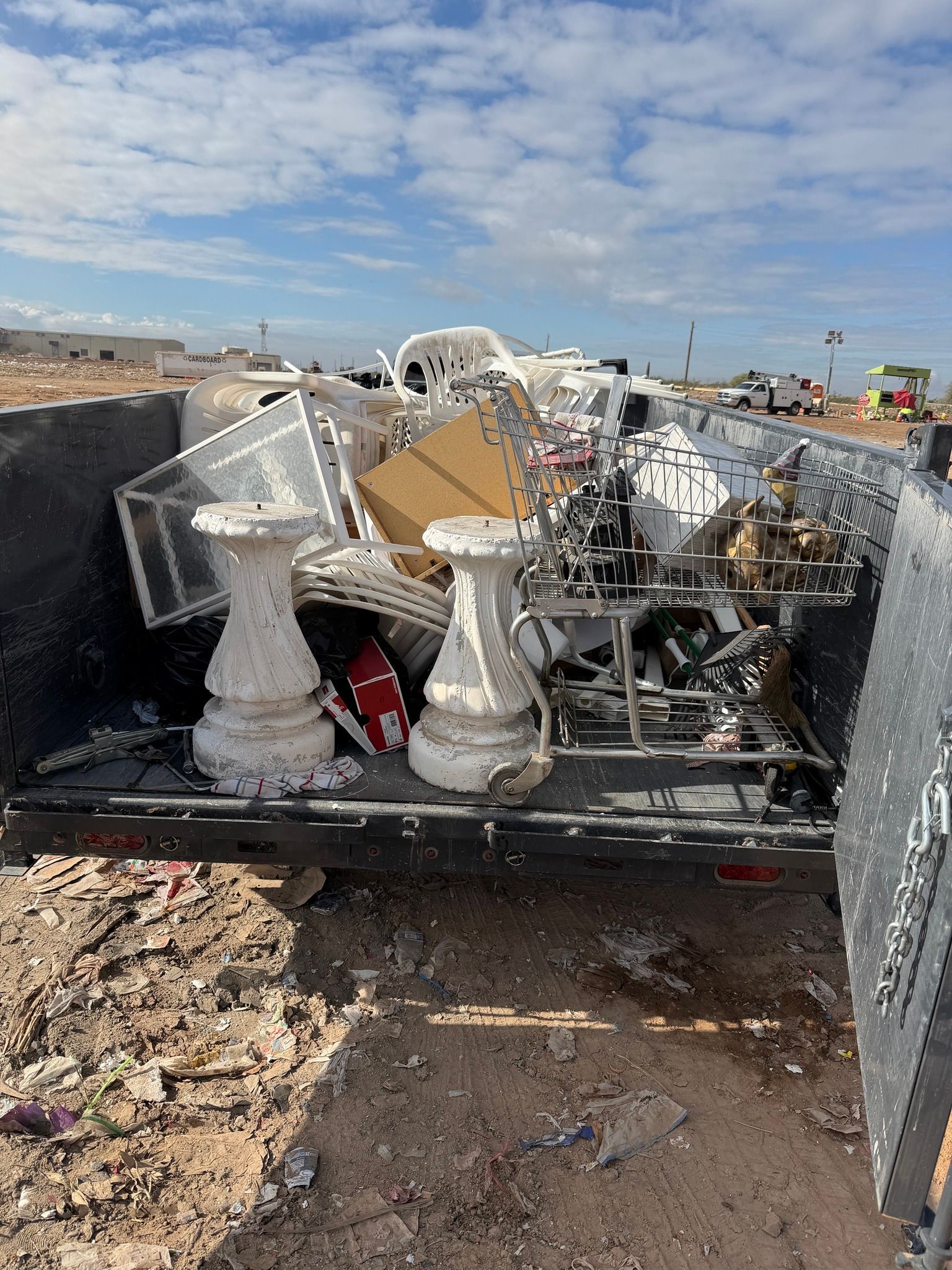 Trailer filled with scrap metal and architectural debris on a dirt lot under a cloudy sky.