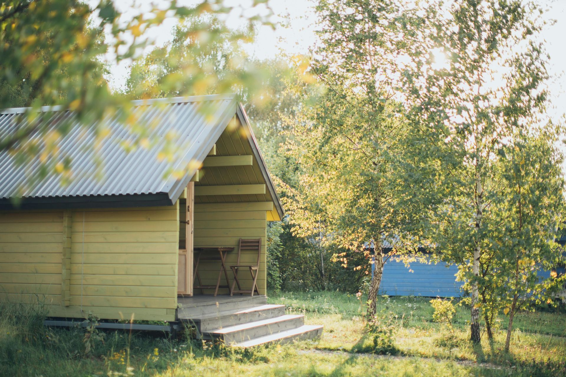 Yellow cabin with porch, surrounded by trees in a sunny outdoor setting.