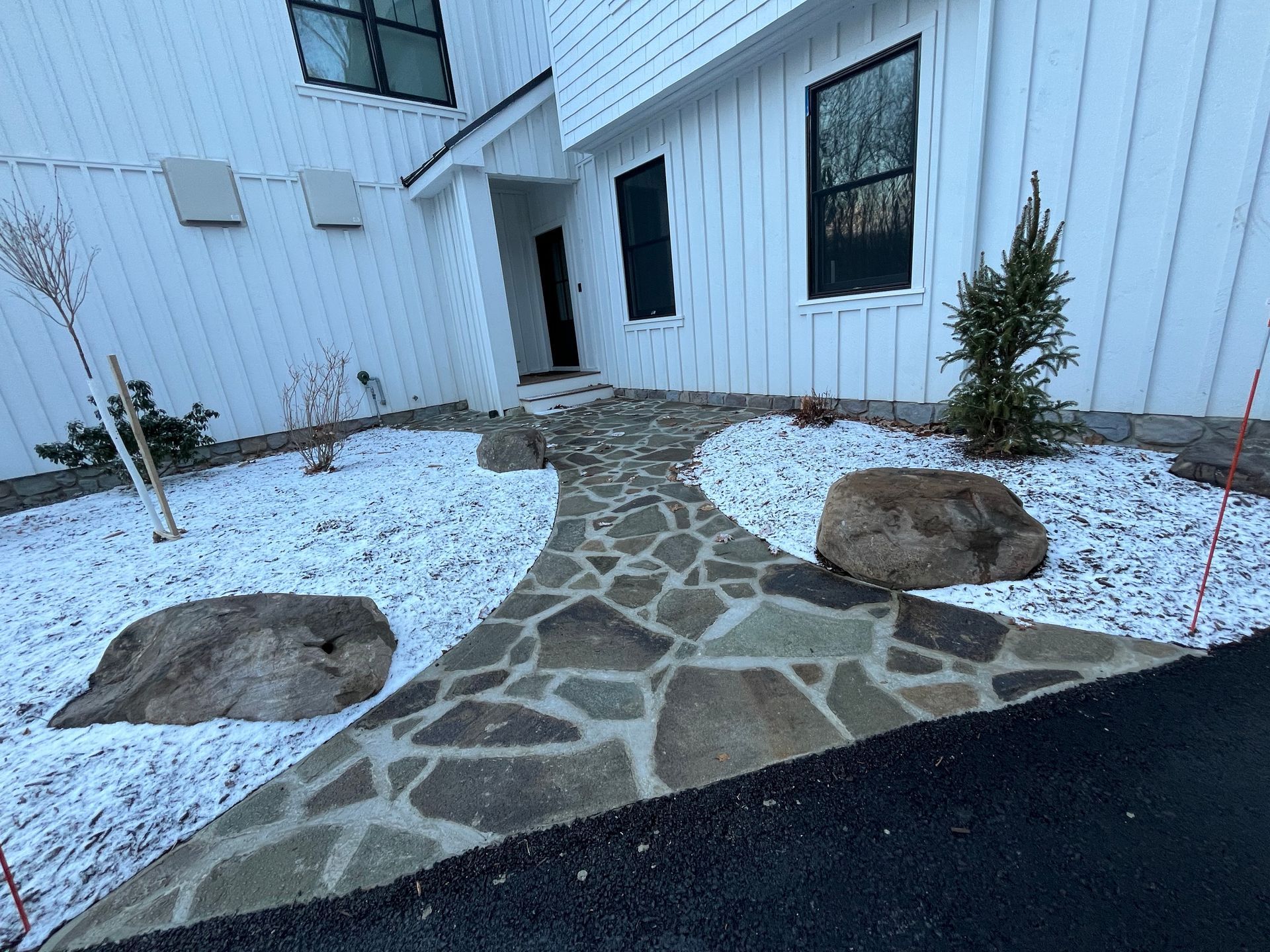 A stone walkway leading to a white house with snow on the ground.