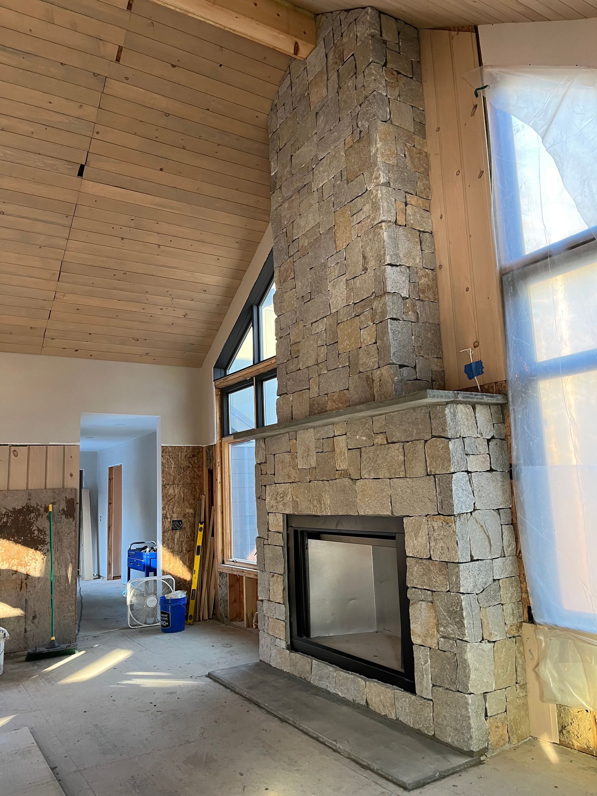 A large stone fireplace in a living room with a wooden ceiling.