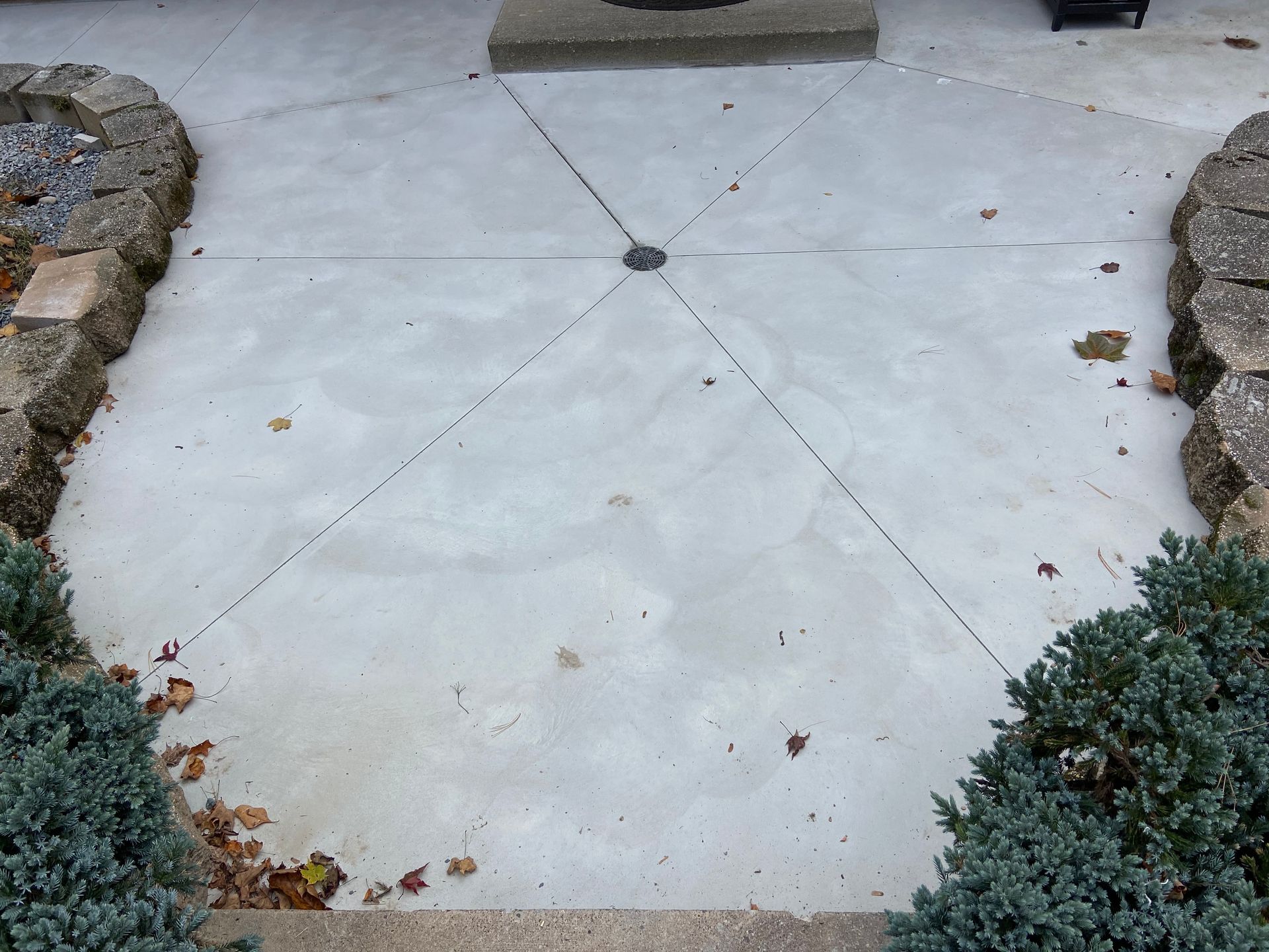 Concrete patio with cracked lines, stone edging, and small bushes.