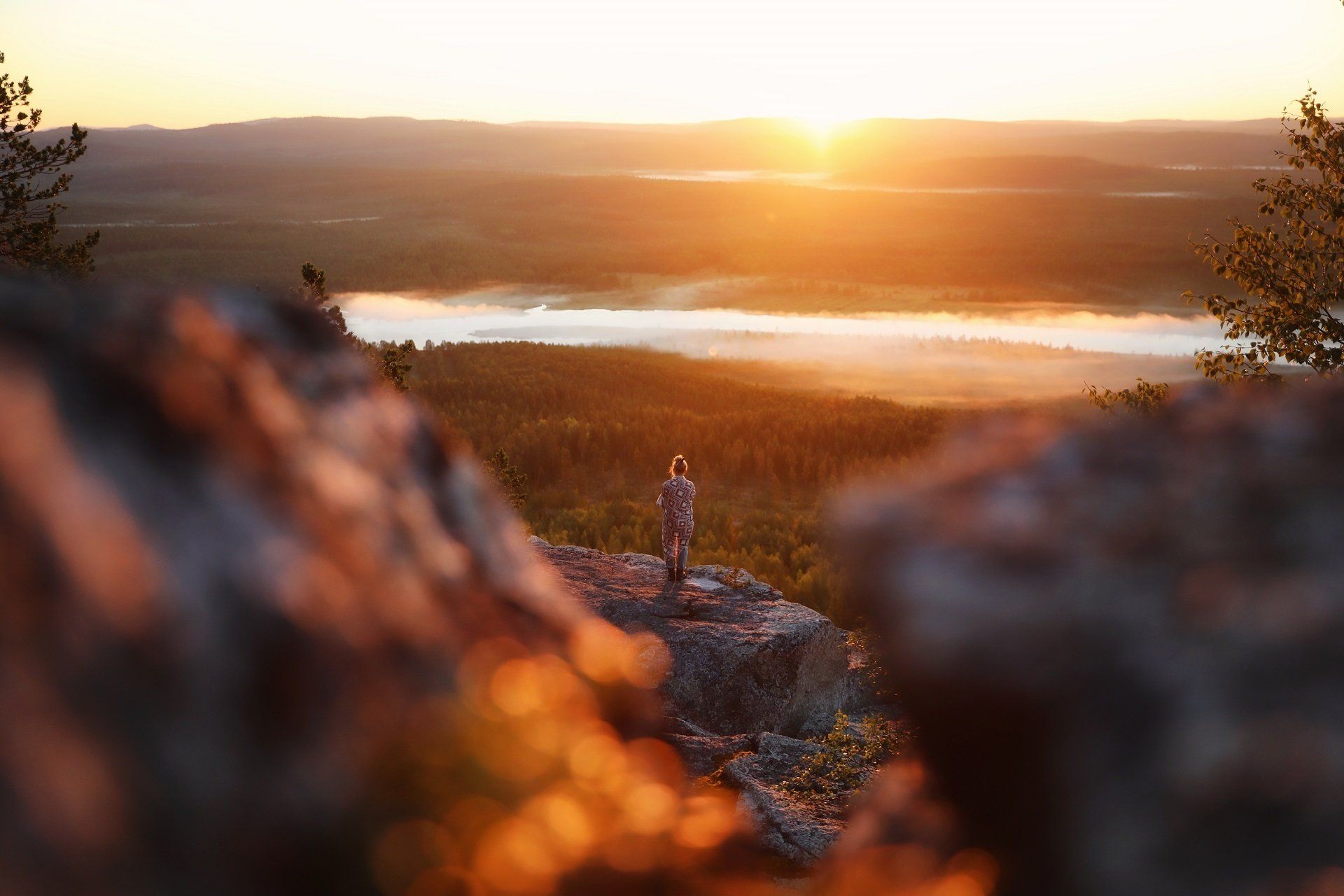 Een persoon staat bij zonsondergang op een rots met uitzicht op een meer.