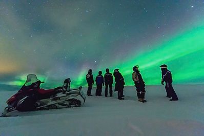 reizigers bewonderen het Noorderlicht tijdens een sneeuwscootersafari