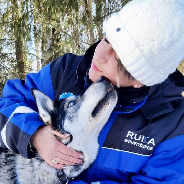 Een vrouw die een blauw jasje draagt ​​waarop 'ruija-avonturen' staat, kust een husky