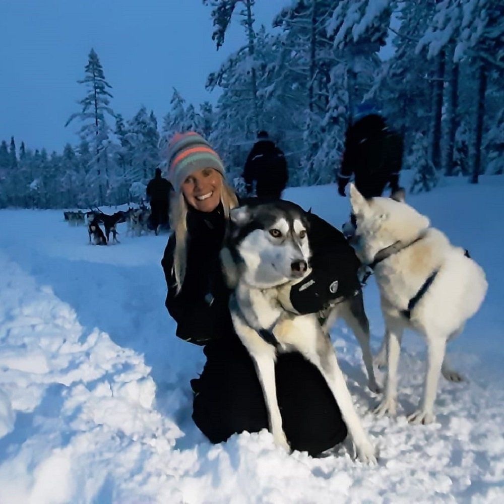 Een vrouw geknield in de sneeuw met een huskyhond in haar armen