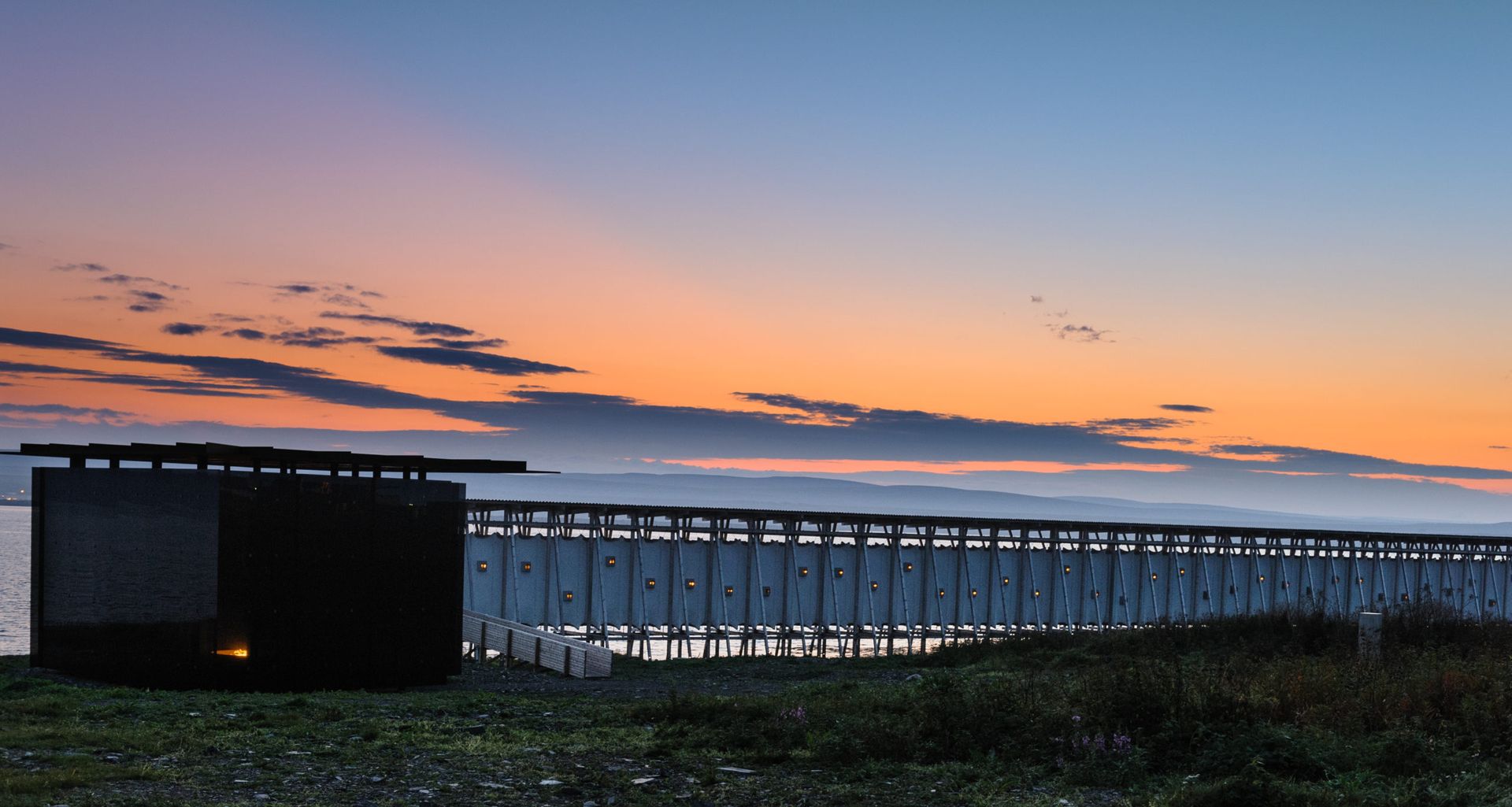 Een zonsondergang boven een watermassa met een gebouw op de voorgrond.