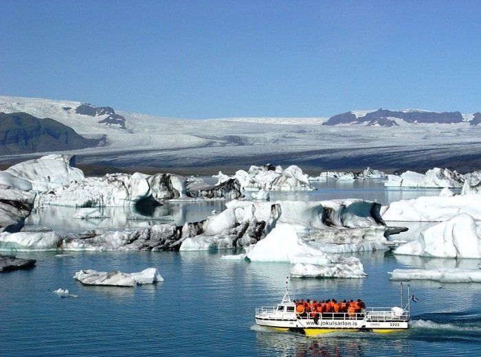 Een boot vol mensen drijft in een watermassa omringd door ijsbergen