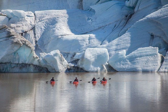 Een groep mensen kajakt in een meer voor een gletsjer.