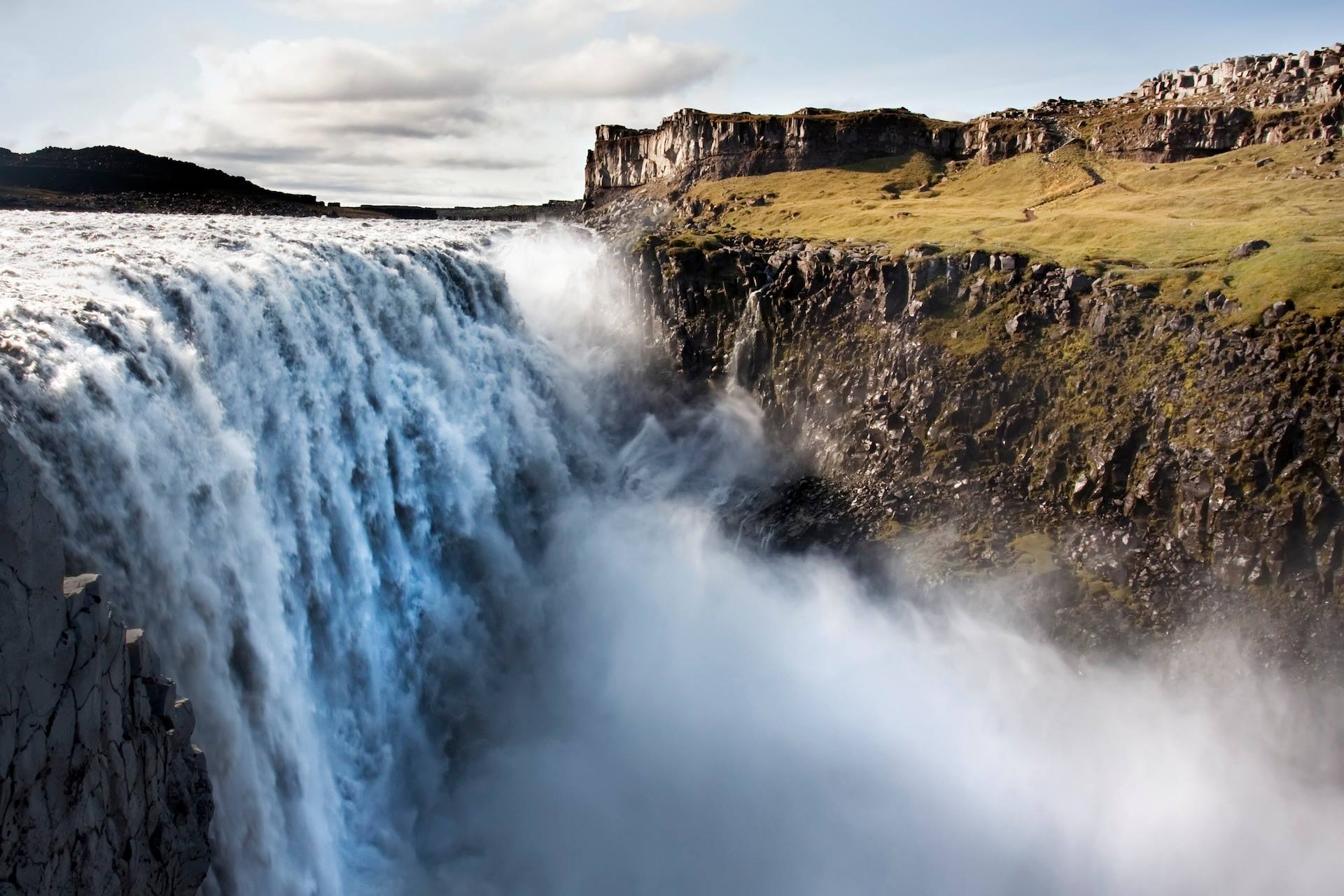 Een waterval midden op een klif waar veel water naar beneden stroomt.