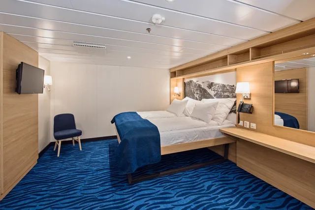 Een hotelkamer met een bed, stoel, televisie en blauw tapijt.