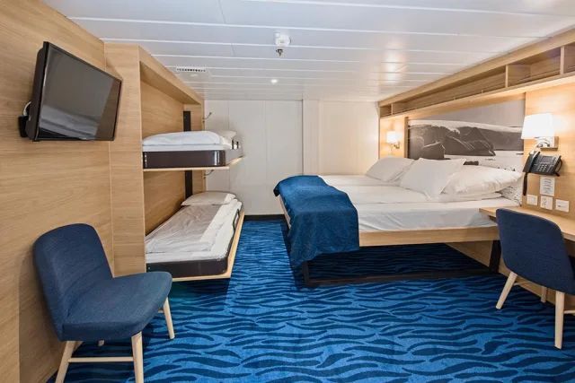 Een cruiseschiphut met twee bedden, een stoel, een bureau en een televisie.