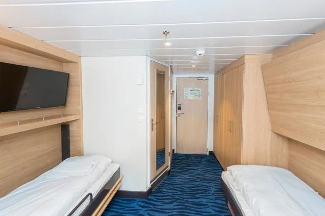 Een kamer met twee bedden en een televisie op een cruiseschip.