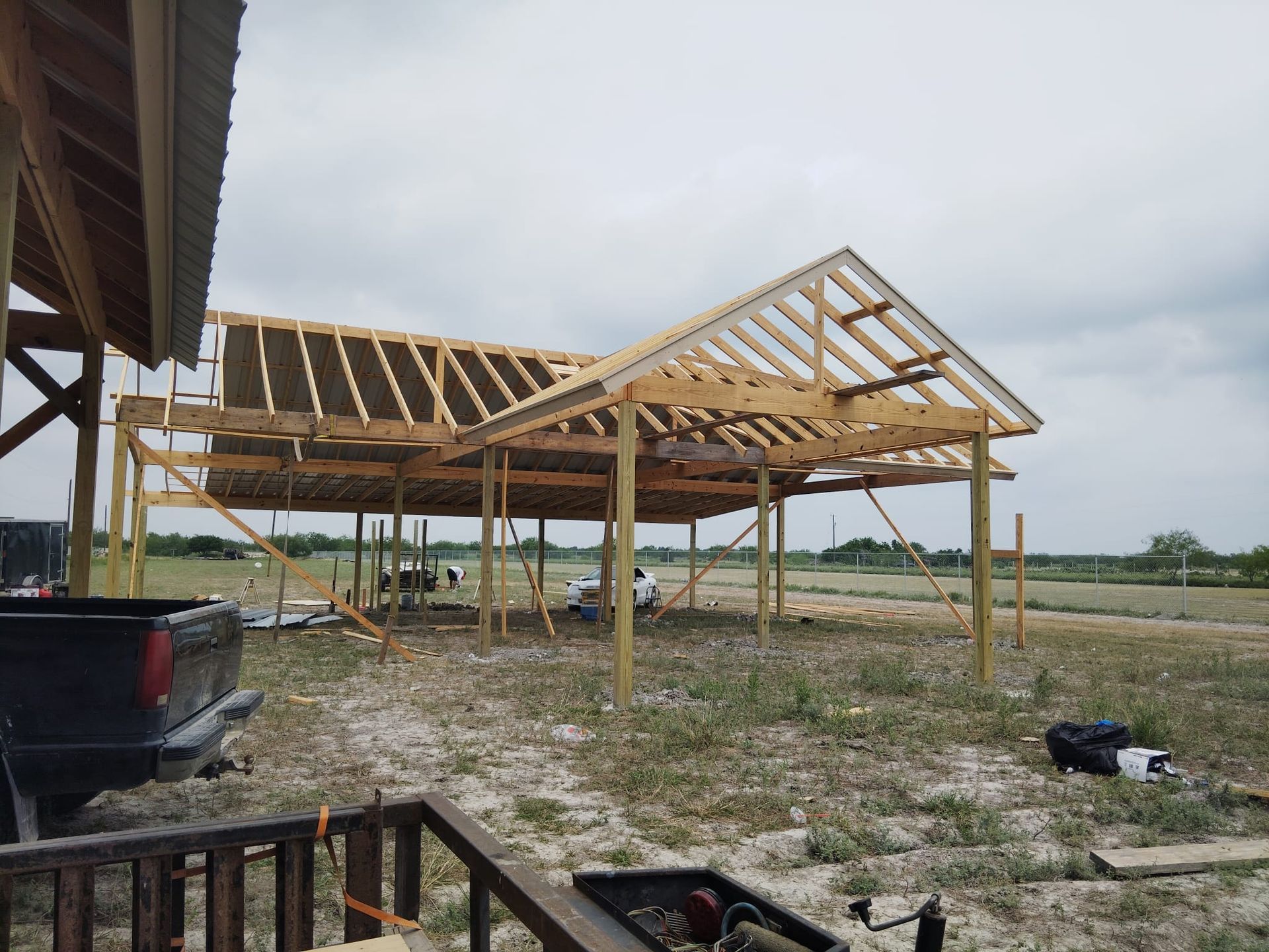 Construction of a wooden building with a gabled roof in a grassy field; a truck is parked nearby.