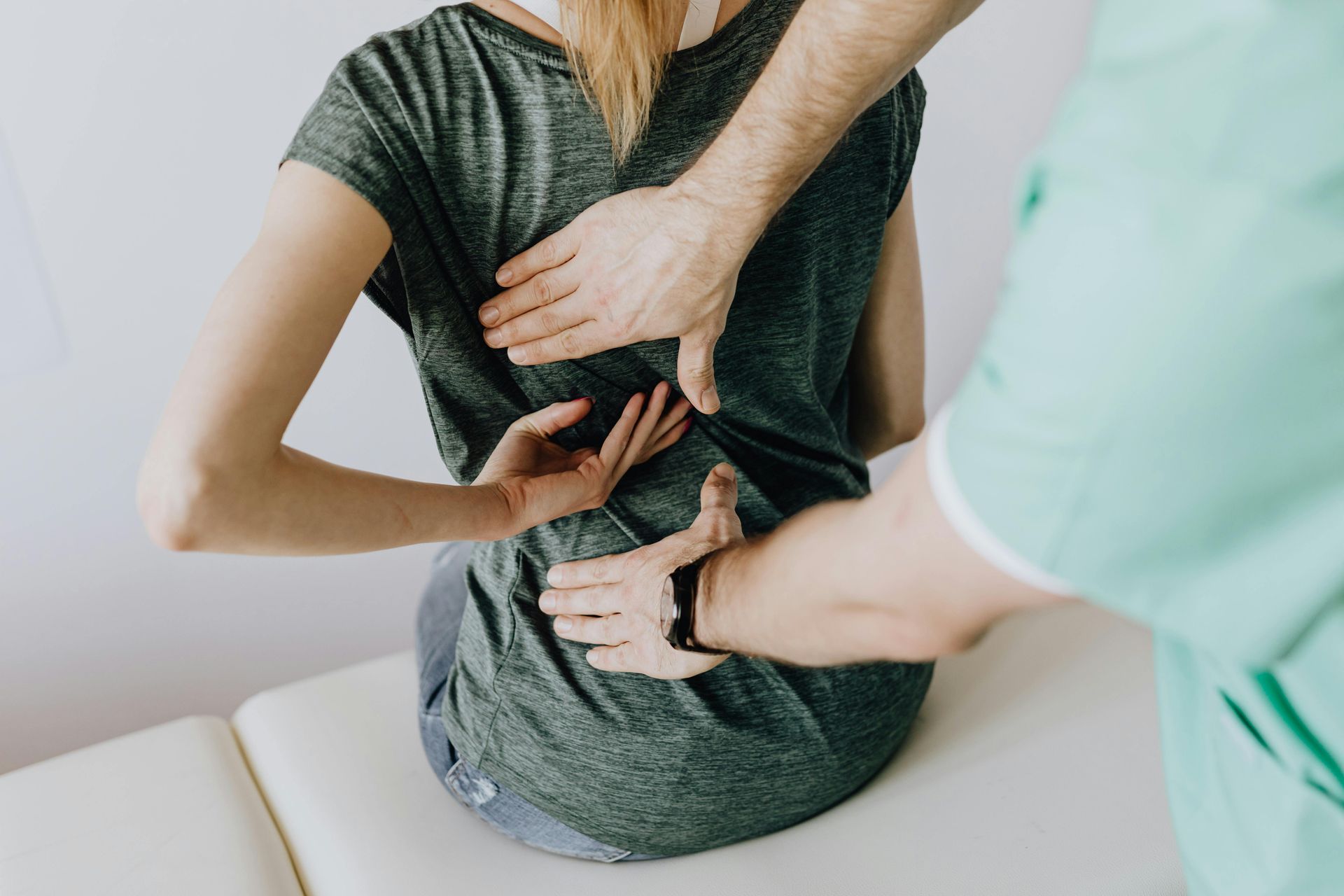 Woman getting her back examined by a doctor. Hands palpate back; white room.