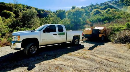 A white truck is parked in a dirt lot next to a machine.