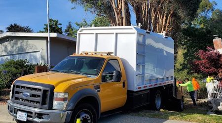 A yellow garbage truck is parked in front of a house.