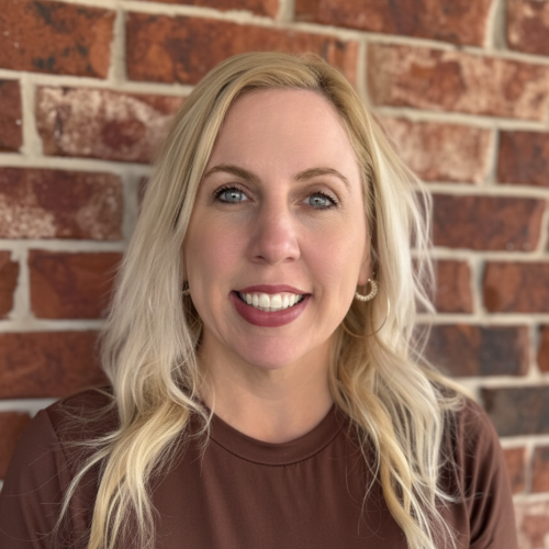 A woman in a red plaid shirt is smiling in front of a brick wall.