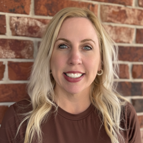 A woman is smiling in front of a brick wall.
