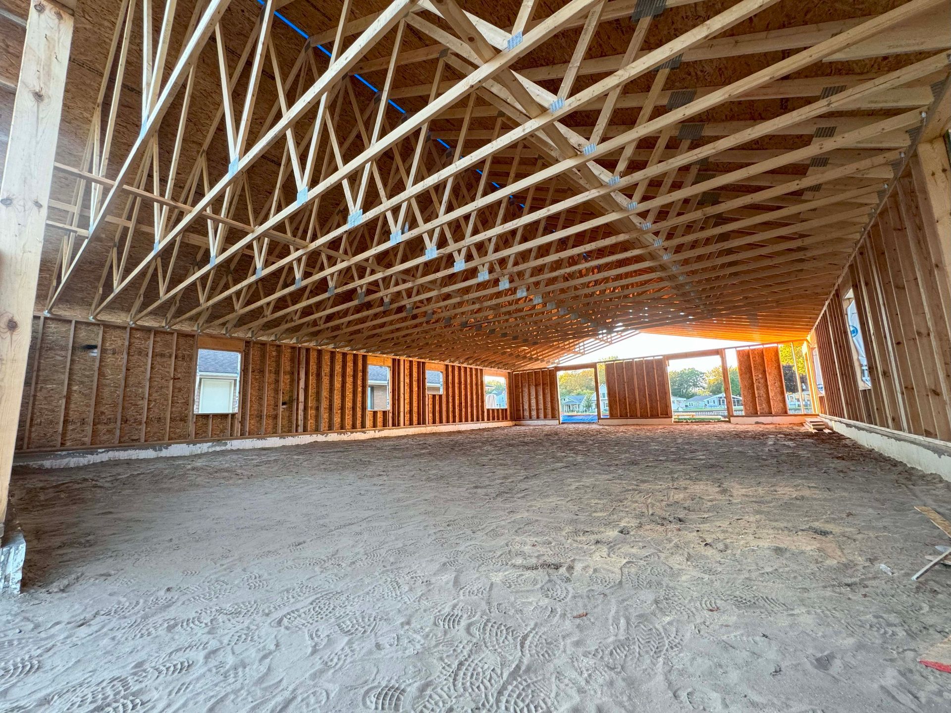 Unfinished building interior with exposed wooden framing, dirt floor, and sunlight streaming through openings.