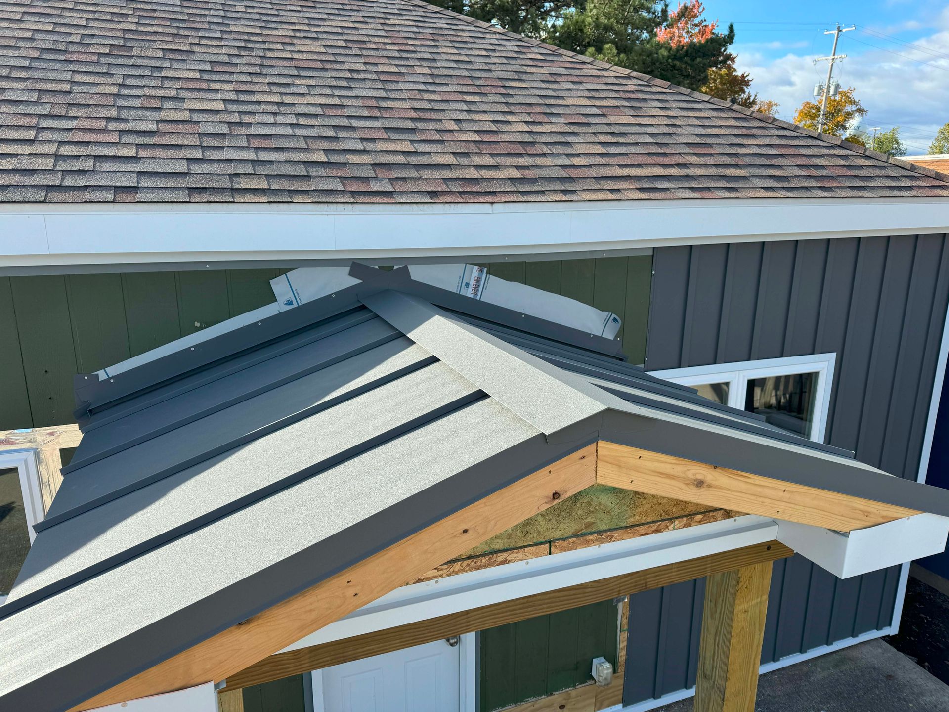 Gray metal awning over a green and gray building, set against a background of a brown shingled roof.