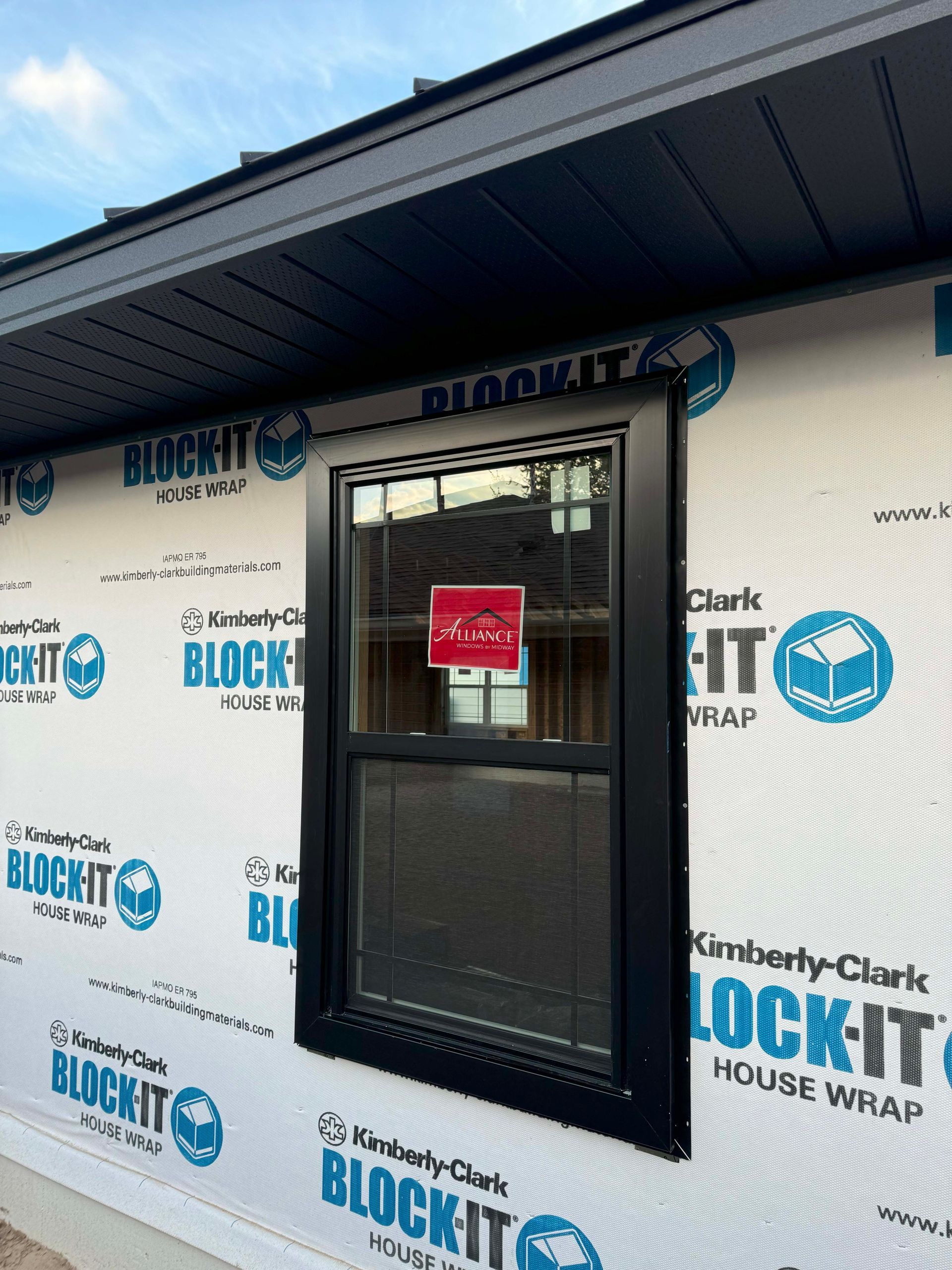Black framed window on a house under construction, with blue and white house wrap visible.