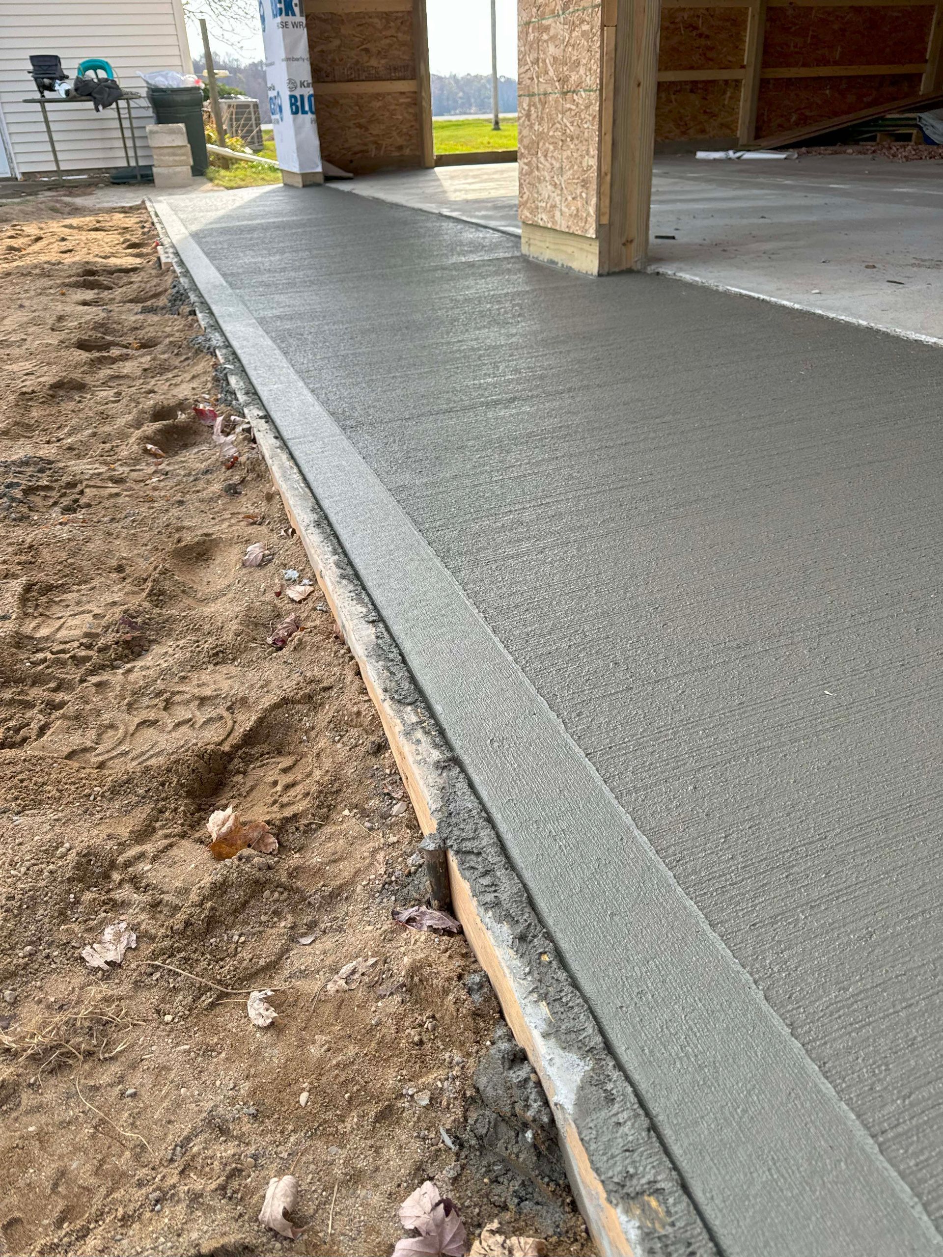 Fresh concrete walkway alongside dirt and a wooden form.