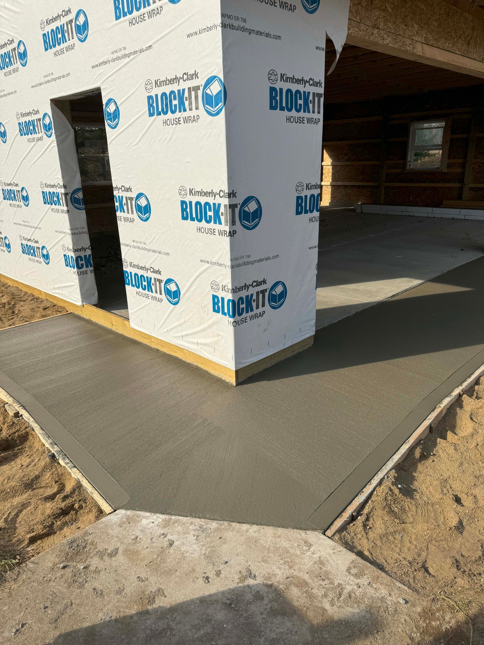 Newly poured concrete pathway and corner of a building, covered in white waterproof wrap.