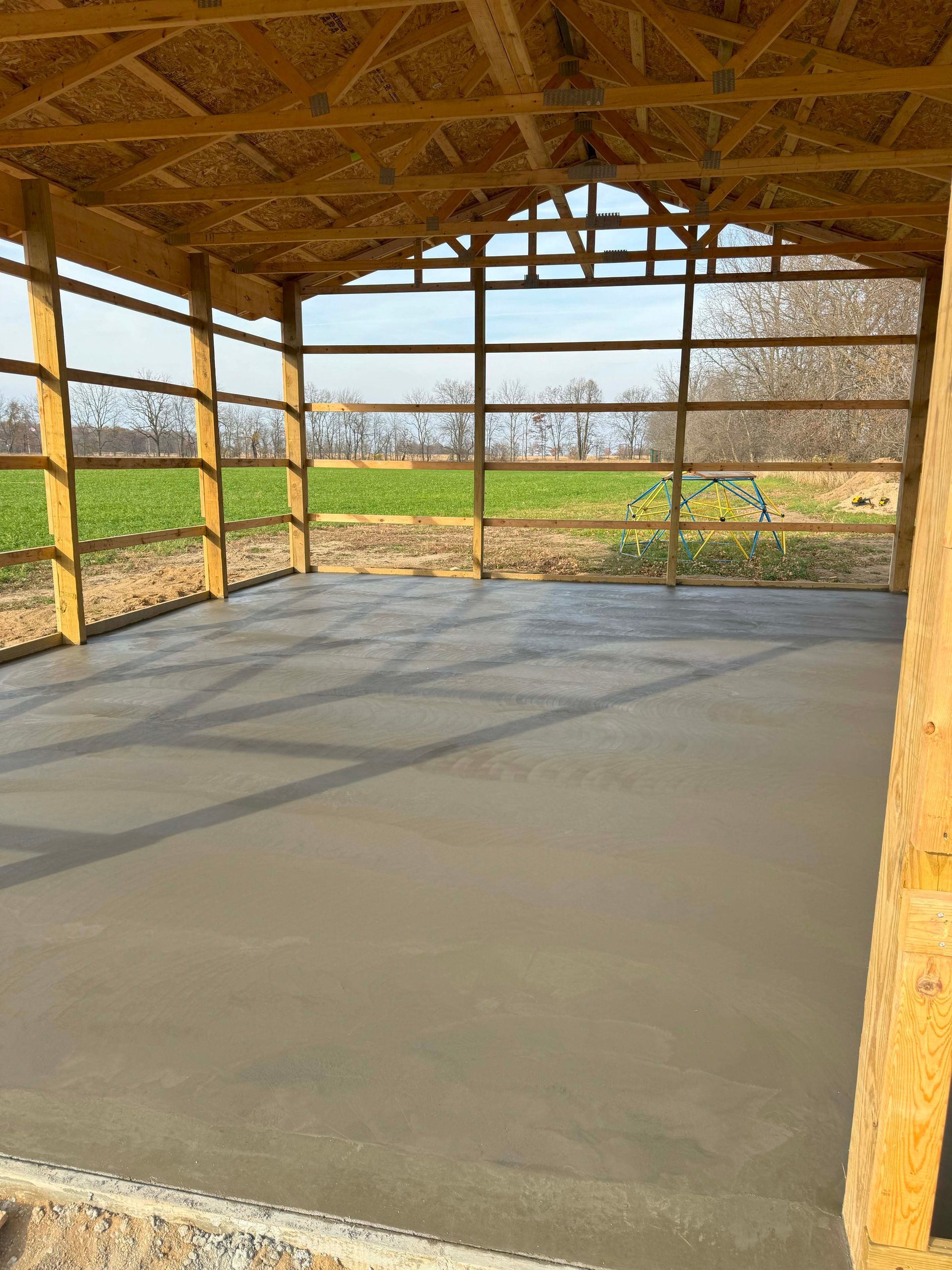 A newly constructed wooden structure with a smooth concrete floor overlooking a field.
