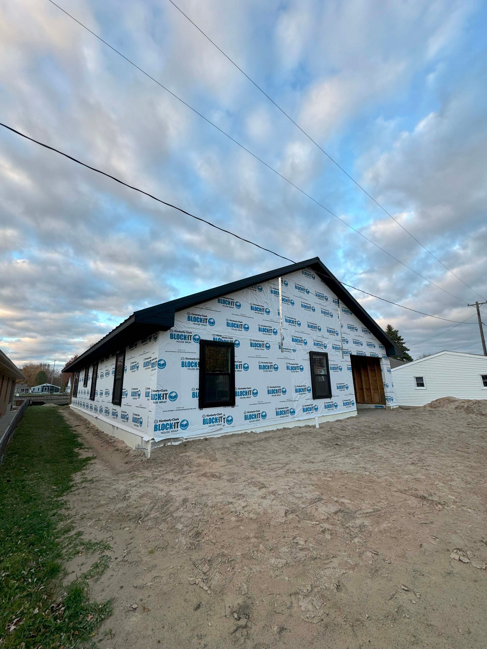 Building under construction; blue wrap, black windows, dirt lot. Cloudy sky.