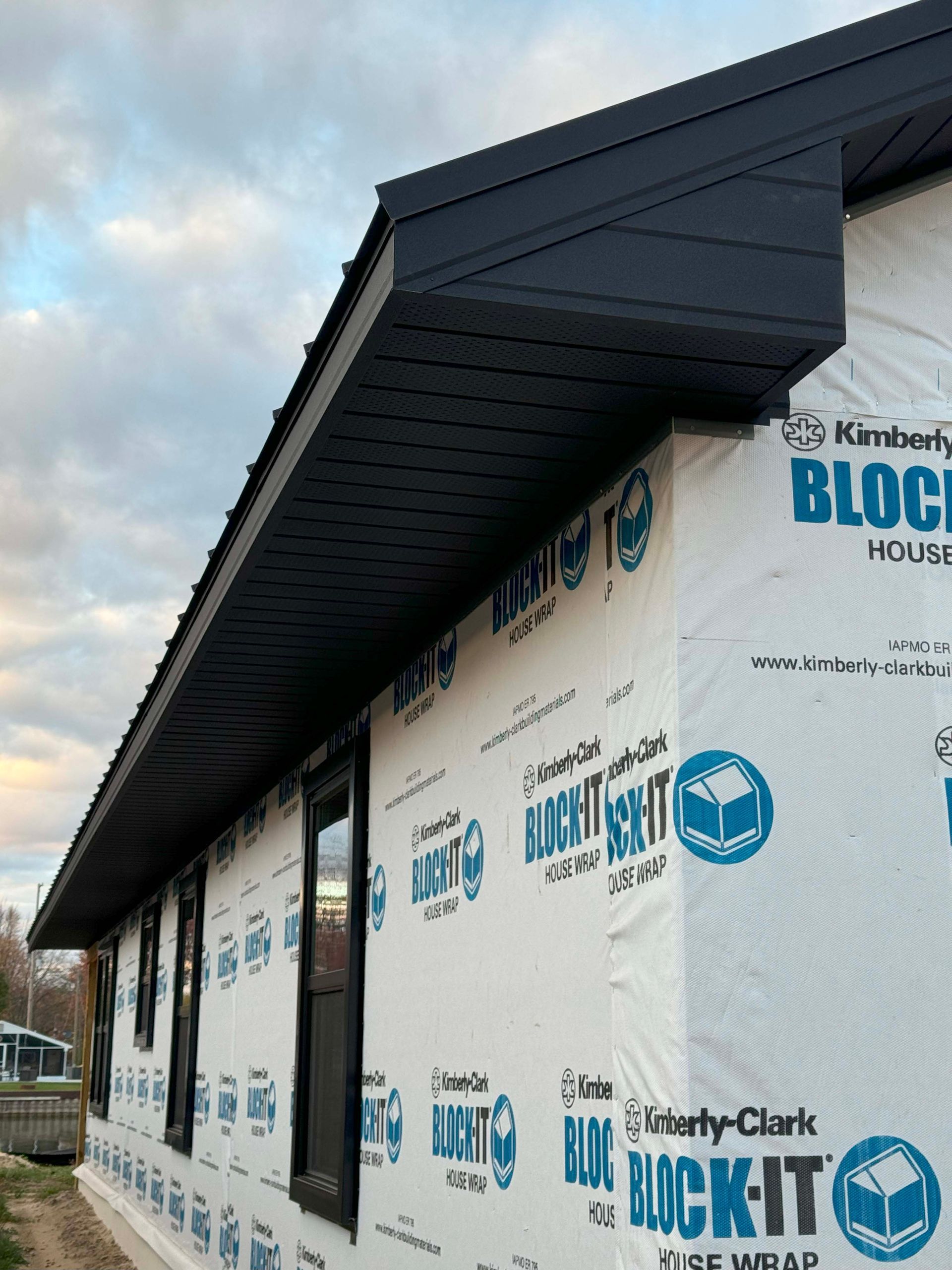 Exterior view of a house under construction with black trim and gray Block-It wrap.
