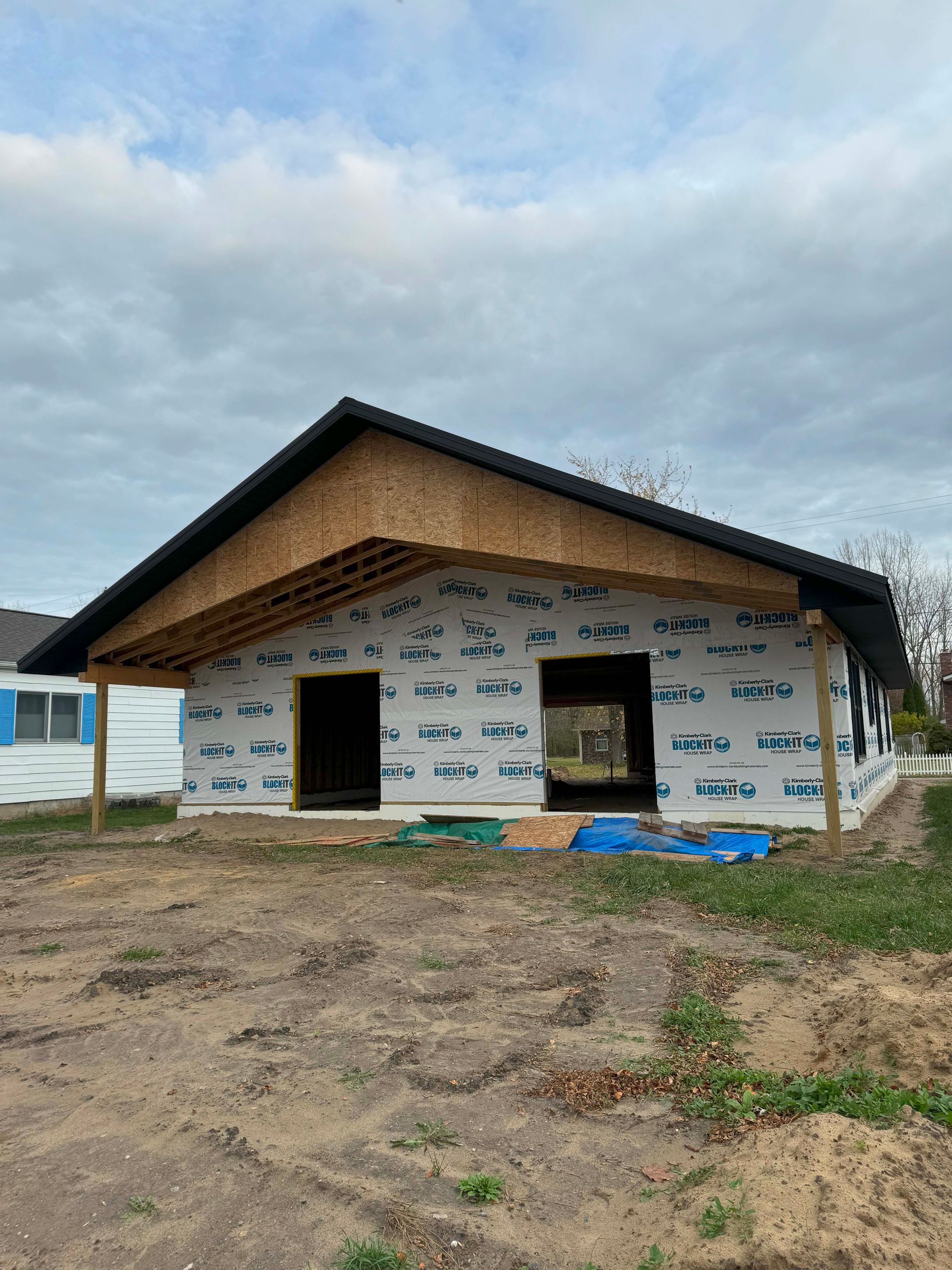 House under construction with dark roof, windows, and blue wrap.