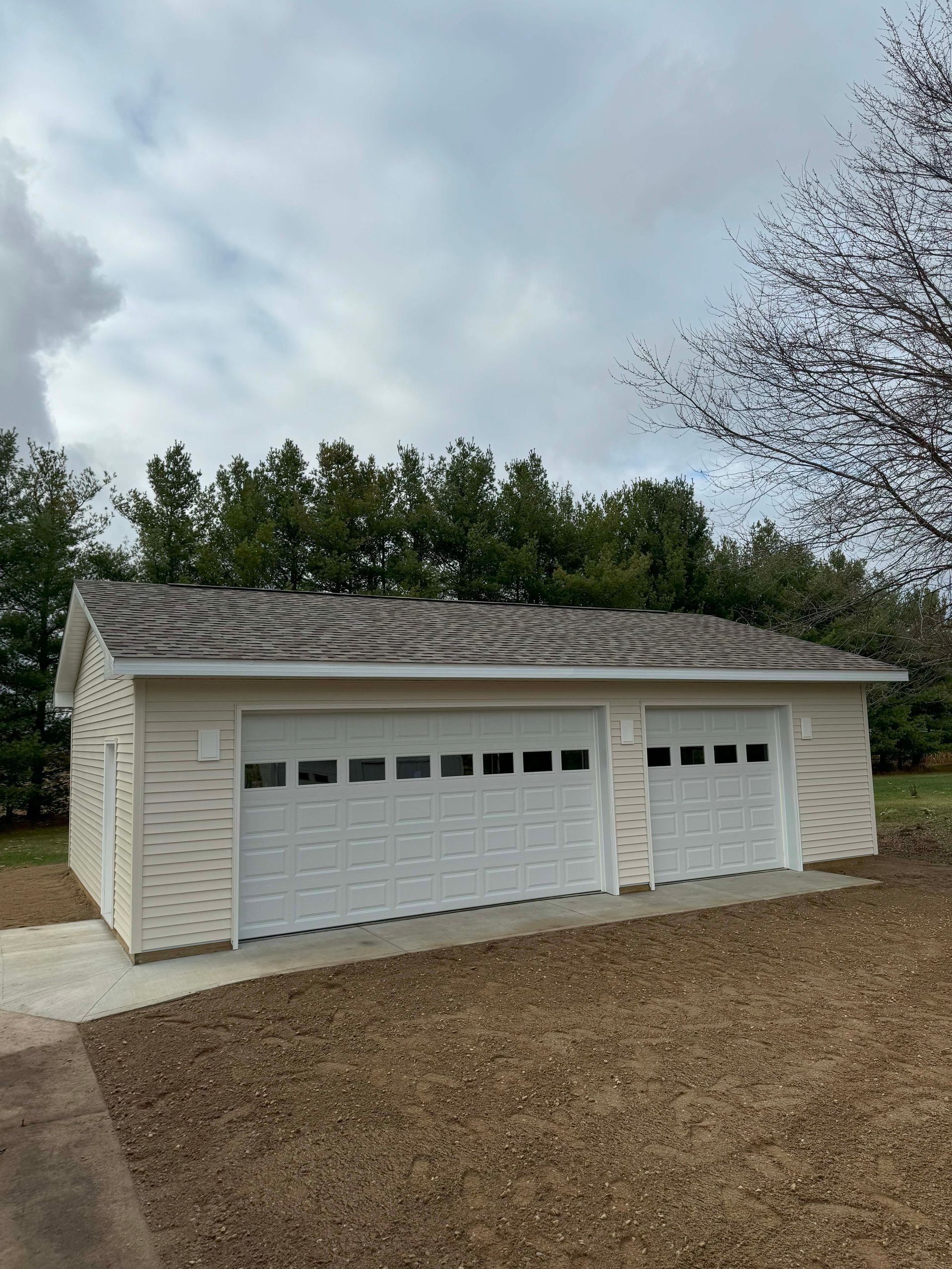 Two-car garage with white doors and tan siding on a cloudy day.