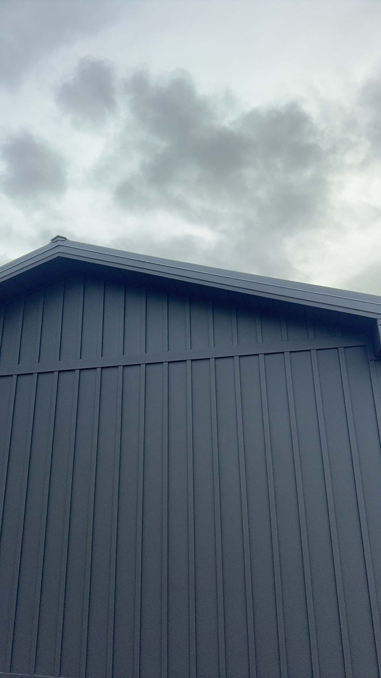 Gray building with a dark roof against an overcast sky.